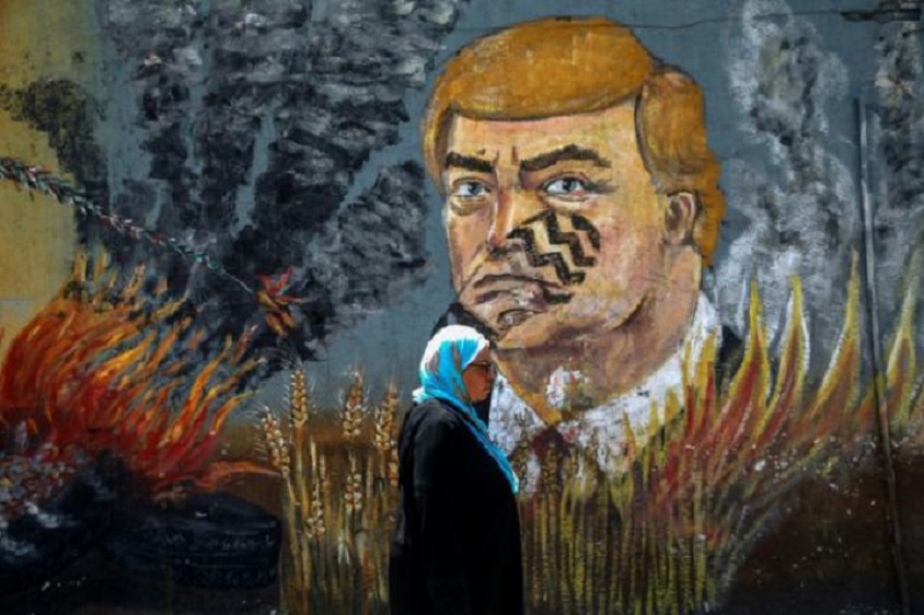 Una mujer palestina pasa por delante de un grafiti que representa a Donald Trump con una pisada en su cara.