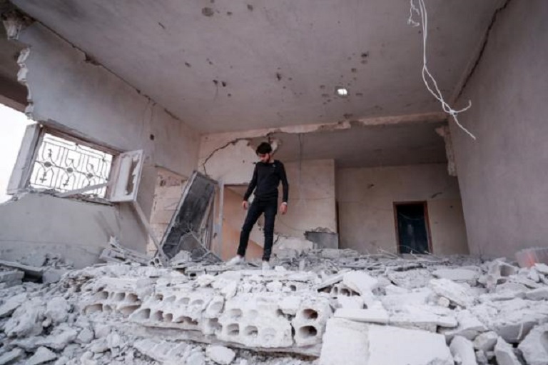 Joven sirio camina sobre los escombros de un edificio destrozado por supuestos ataques aéreos.