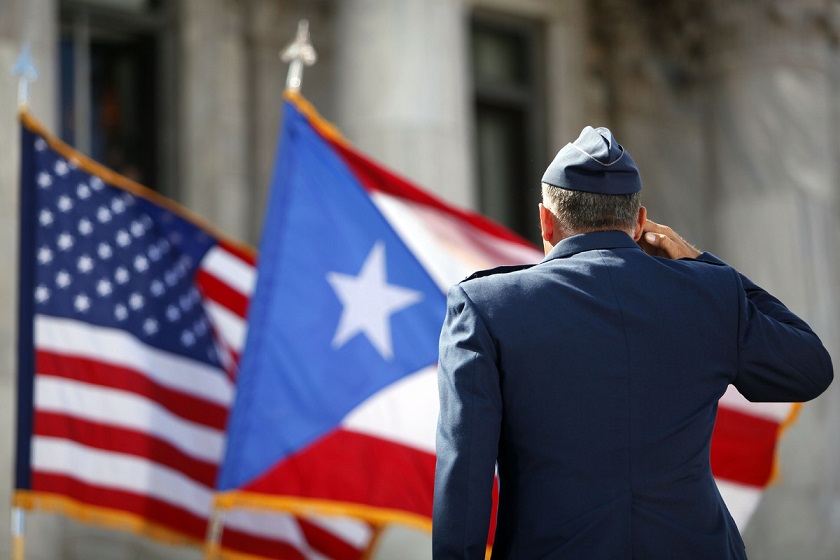 Miembro del Ejército rinde homenaje a banderas de Estados Unidos y Puerto Rico.